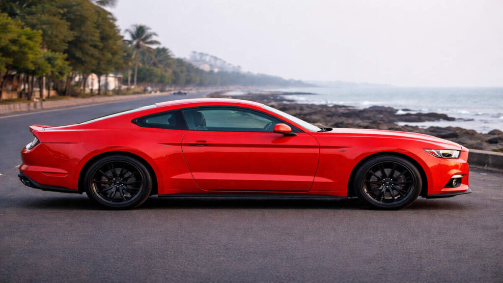 Side profile view of Ford Mustang in Race Red parked near a coastal road